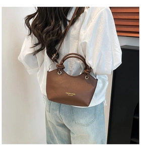 Brown leather crossbody bucket bag with knotted handle detail shown on a model