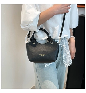 Detail of black pebbled leather bucket bag with gold lettering and top handle