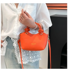Detail of bright orange lychee grain leather bucket bag with decorative knotted handle