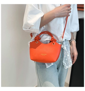 Detail view of mini orange leather bucket bag with top handle and golden hardware buckle