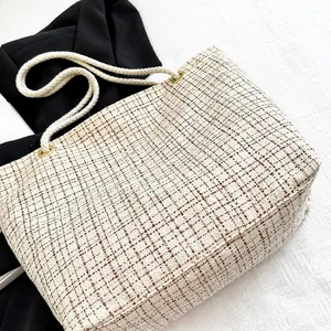 Detail view of large beige tweed tote bag with red checkered pattern and rope handles