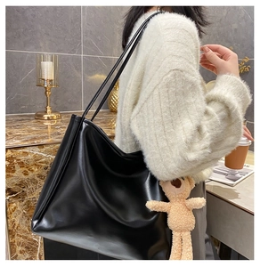 Detail view of a large black tote bag with slender straps and a cute beige bear charm