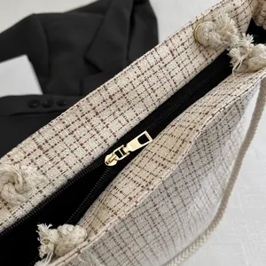 Detail of tweed tote bag showing golden zipper closure and braided rope handle knots