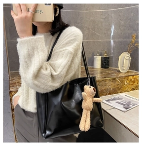 Close-up of a black tote bag with a beige teddy bear pendant and slim shoulder straps
