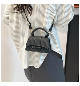 Detail of a black textured crossbody bag with a curved base and top handle