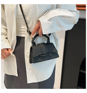 Detail of a mini black woven handbag featuring a top handle and adjustable shoulder strap