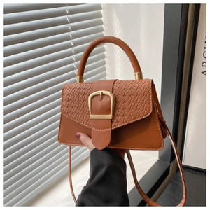 Close-up of caramel brown square bag featuring woven leather flap and gold buckle