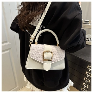 Detailed shot of white crossbody bag featuring woven flap and large gold U-shaped buckle