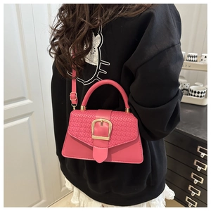 Detail of pink woven leather flap handbag featuring a bold gold horseshoe buckle