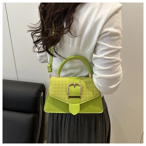 Detail of green crossbody bag with woven texture lid and large gold buckle accent