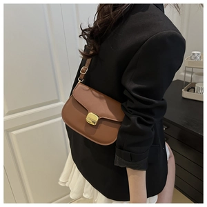 Sac besace en cuir marron avec boucle dorée porté par un mannequin en décor minimaliste