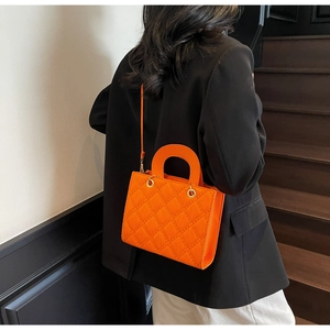 Detail of bright orange quilted crossbody bag with top handle worn with black blazer