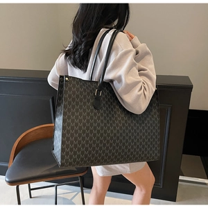 Detailed view of black tote bag with gray M-letter pattern and leather strap