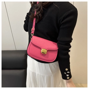 Détail d'un sac besace rose en cuir avec boucle dorée porté sur une jupe plissée