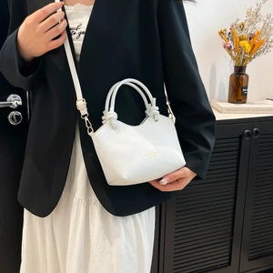 Minimalist white leather bucket bag with knotted handle shown with elegant outfit