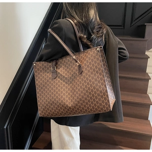 Detail of vintage brown tote bag with M-pattern and leather handles on model shoulder