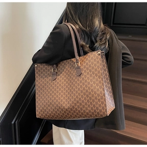 Detail of a large retro tote bag with brown 'M' monogram pattern on a model's shoulder
