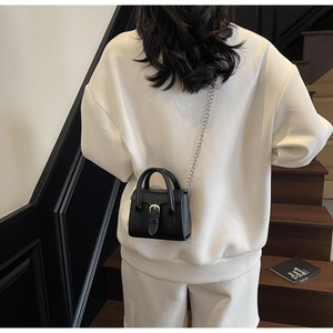 Close-up of minimalist black square bag with silver chain strap worn by a model