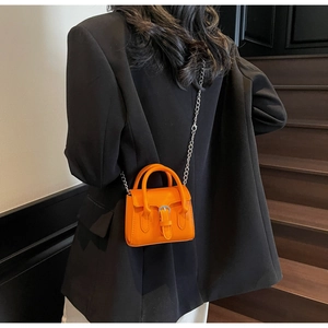 Mini orange leather crossbody bag with silver buckle and chain on black blazer