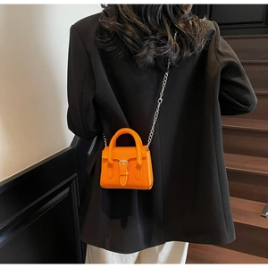 Détail du mini sac orange avec chaîne argentée porté sur un blazer noir élégant