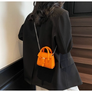 Gros plan d'un sac carré orange vif avec bandoulière en chaîne et boucle argentée