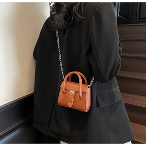 Petit sac carré marron avec chaîne sur un blazer noir pour un style rétro chic