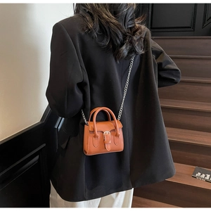 Detail of a chic orange mini crossbody bag with silver chain strap worn by a model