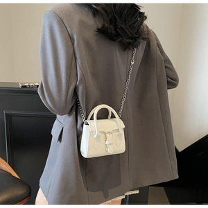 Détail du mini sac blanc à poignées rondes et chaîne porté sur un blazer gris