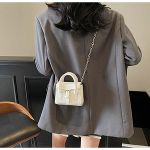 Detail of white mini crossbody bag with glossy finish and silver chain on a grey blazer