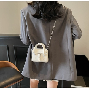 Gros plan d'un mini sac à main blanc carré avec bandoulière chaîne et blazer gris