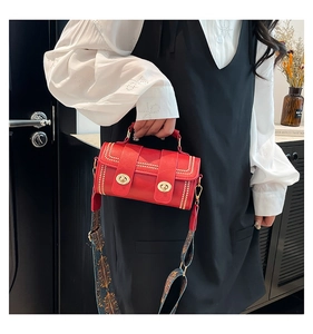 Detail of red textured leather handbag with gold twist locks and ethnic print wide strap