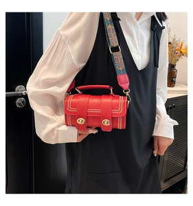 Detail of red cylinder bag with gold studs and colorful ethnic wide strap on model