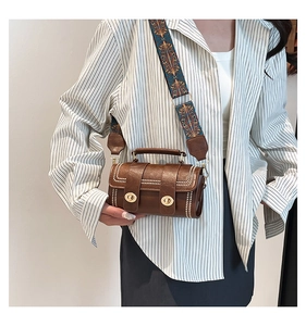 Brown cylinder handbag with wide patterned strap and studded detail worn by model