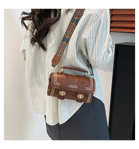 Detail of brown barrel crossbody bag with white stitching and colorful woven strap