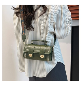 Detail view of a green cylinder bag with golden clasps and a bohemian style wide strap