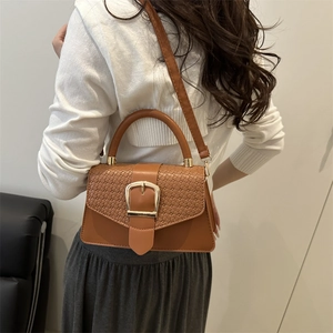 Caramel brown square shoulder bag with woven flap and gold buckle on a fashion model