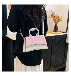 Close-up of pink and white crossbody bag with metal handle styled on a model in a home setting