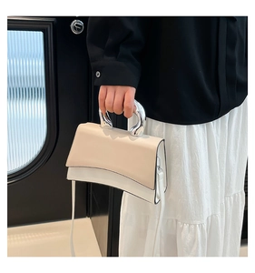 Detail of minimalist beige handbag with curved silver metal handle and shoulder strap