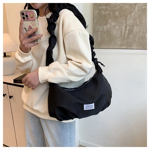 Detail of a black nylon crossbody bag with ruffled strap and 'FASHION' label design