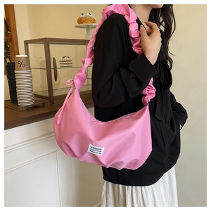 Detail of pink ruched shoulder bag with ruffled strap and fashion label on soft silk fabric