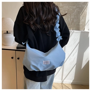 Detail of light blue crescent bag with ruched strap worn by a model in a sunlit room