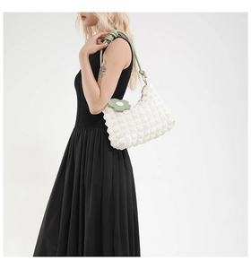 Detail of white quilted cloud bag with green knotted strap and floral pendant on black dress