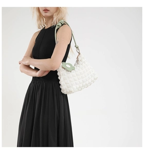 Detail of cream pleated crossbody bag with green knotted strap and daisy charm on a model