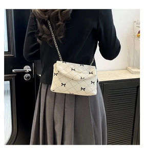 Detailed shot of beige quilted corduroy crossbody bag with black bow patterns and chain strap
