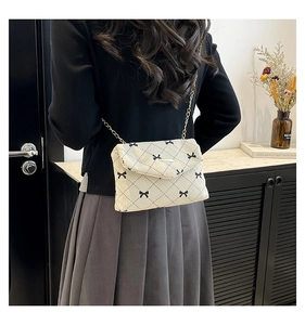 Detail view of beige corduroy envelope bag with black bow patterns and gold chain strap