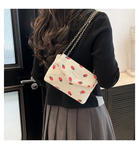 Detail of corduroy crossbody bag featuring red strawberry prints and gold chain strap