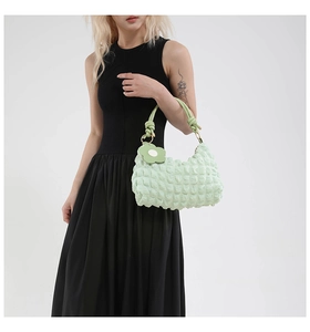 Detail of light green quilted bubble texture handbag with knotted strap and flower charm