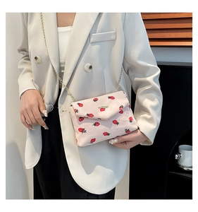 Detailed texture of pink corduroy shoulder bag with red strawberry print and gold chain