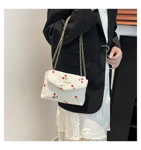 Detailed texture of white corduroy shoulder bag with red cherry embroidery and chain strap