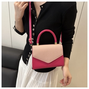 Detail of rose red crossbody bag with beige woven flap on model's white skirt